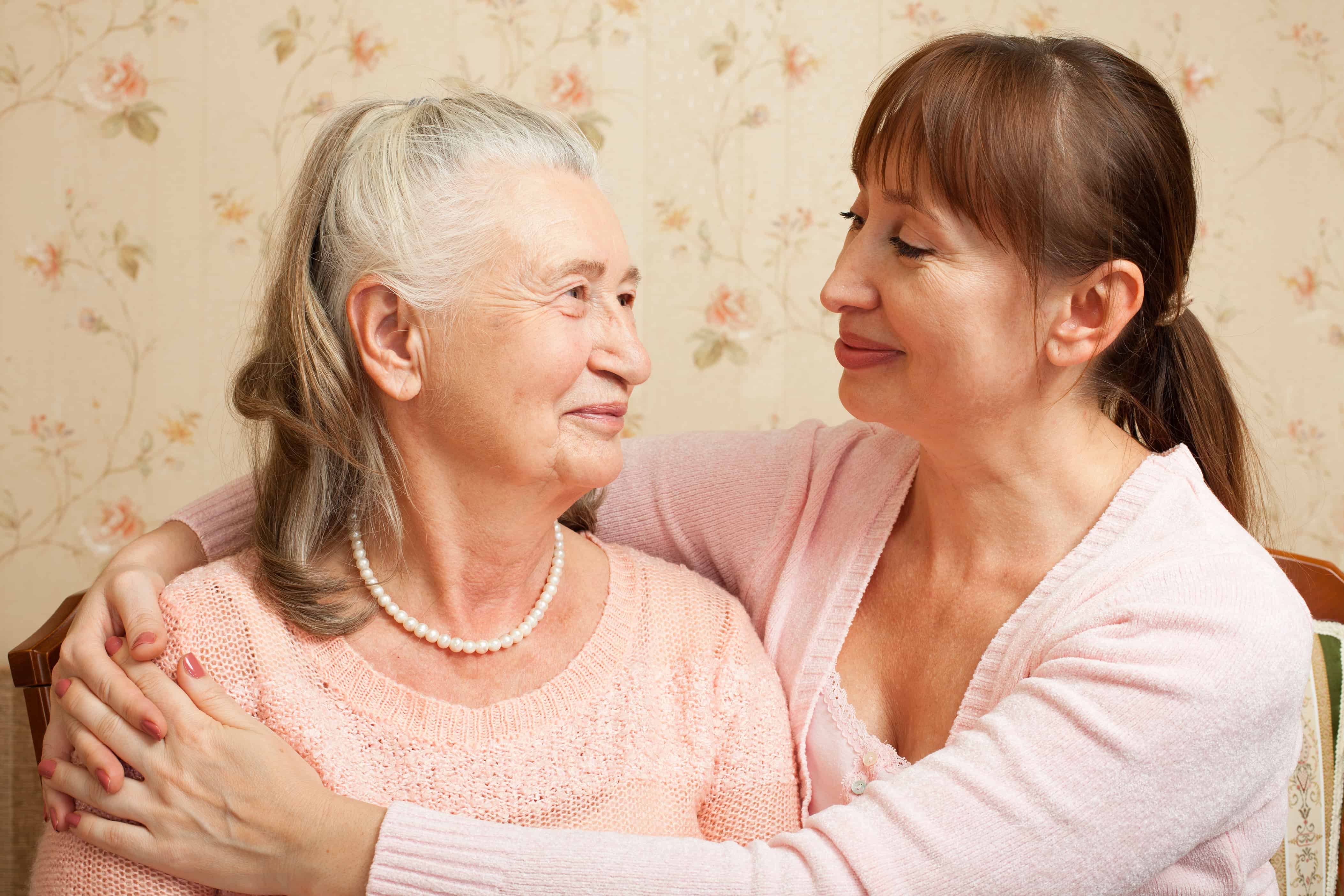Happy family. Portrait of elderly woman and adult daughter happily looking at camera. Senior woman with their caregiver at home.